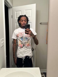 a man with dreadlocks taking a selfie in a bathroom mirror while looking at his cell phone