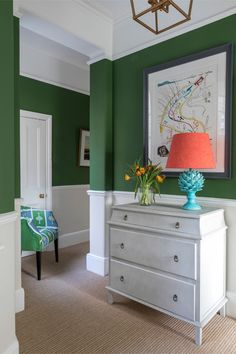 a bedroom with green walls and white dresser in the foreground is a painting on the wall