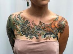 a woman with tattoos on her chest is looking up at the sky and has an orange fox