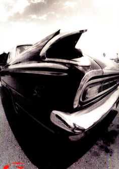 a black and white photo of an old car with the hood open, parked in a parking lot