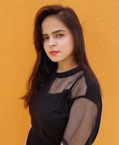 a woman standing in front of a yellow wall with her hands on her hips and looking at the camera