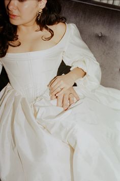 a woman in a white dress sitting on a couch with her hand on the pillow