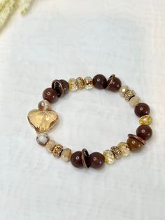 Our New Bonbon Bracelet is a stunning single bracelet with lots of eye catching details. From the ambient  toasted heart as the centerpiece, to the 10mm Creamy chocolate quartz beads. Perfect for fall and winter cozy date nights to casual days in the earthy brown is comforting. Affordable Brown Jewelry With Gold Beads, Cheap Brown Stretch Bracelet For Gift, Elegant Luxury Brown Beads, Brown Accessories Aesthetic, Luxury Brown Beaded Bracelets With Gemstone, Brown Bracelet Aesthetic, Bohemian Heart-shaped Beaded Bracelets, Bohemian Heart Bracelet With Colorful Round Beads, Elegant Heart-shaped Bracelets With Colorful Beads