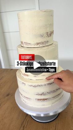 a three tiered cake sitting on top of a wooden table next to a hand holding a sticker