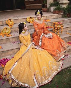 two brides sitting on the steps in orange and yellow dresses with flowers around them