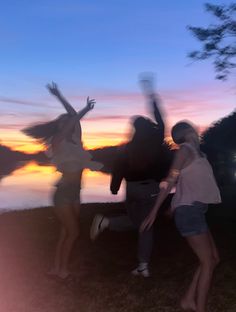 three people are dancing in front of the water at sunset