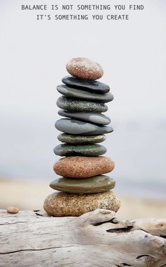 a stack of rocks sitting on top of a wooden log next to the ocean with a quote above it