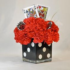 red carnations and white polka dots in a black vase with playing cards on top