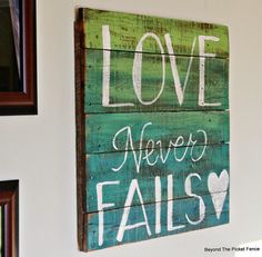 a wooden sign that says love never falls on the side of a wall with pictures hanging above it