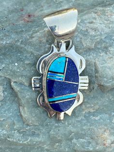 This beautifully well crafted Oval Pendant has been handmade by a Navajo Artisan. The Colors of the Pendant come from Lapis Lazuli, Turquoise and Blue Opal. The Pendant measures 1.5 long and 7/8 wide. It is stamped Sterling and signed by the Artist. Winds of Wisdom (Lapis Lazuli, Turquoise and Blue Opal. The Navajo (Dine) believe that the wind is a powerful source. The native tradition believes that at any moment, the blowing wind can inspire one with hope, resolve, and great wisdom. Wisdom has Southwestern Blue Oval Jewelry, Blue Oval Southwestern Jewelry, Oval Blue Southwestern Jewelry, Southwestern Style Blue Oval Jewelry, Southwestern Blue Oval Pendant Jewelry, Handmade Southwestern Blue Jewelry, Artisan Oval Blue Jewelry, Traditional Oval Blue Jewelry, Blue Bohemian Jewelry With Inlay