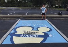 a man standing on the side of a parking lot next to a mickey mouse sign