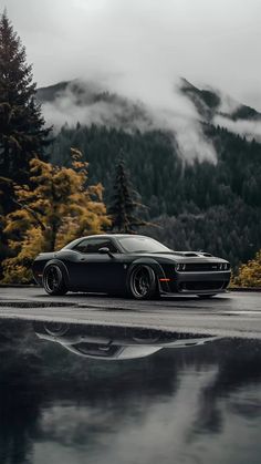 a black sports car parked in front of a mountain with trees and clouds behind it