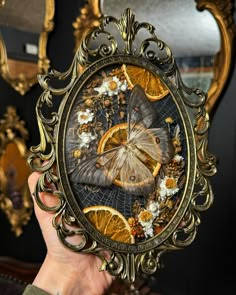 a person holding up a painting in front of a mirror with oranges and butterflies on it