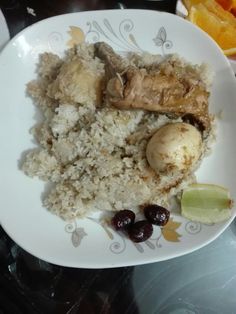 a white plate topped with rice and meat next to orange wedges on a table