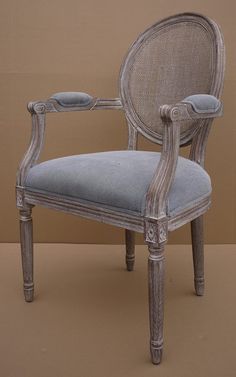 an old chair with blue upholstered seat and arm rests against a brown wall