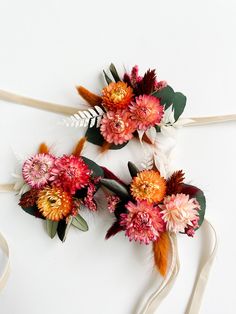 two flowers are tied to ribbons on a white surface, one is orange and the other is pink