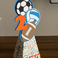 a paper toy with a football and soccer ball on it's head sitting on a table