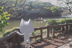 a white cat statue sitting on the side of a wooden fence next to a river