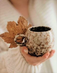 a woman holding a coffee mug in her hand with a leaf on the top and bottom