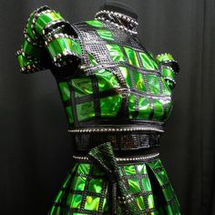 a green and black dress on display in front of a black background with silver studded accents