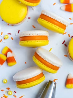 there are many candy macaroons on the white surface with orange and yellow icing