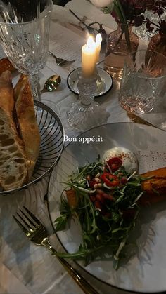 there is a plate with bread and salad on it next to a glass candle holder