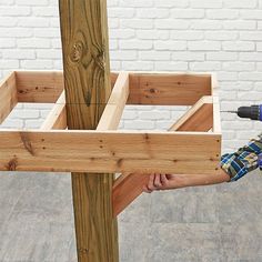 a man holding a drill in his hand next to a wooden structure with two pieces of wood