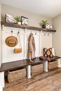 a wooden bench with baskets underneath it and coat rack on the wall behind it, along with two coats hanging from hooks