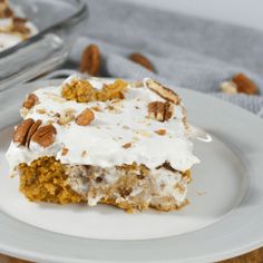 a piece of cake on a white plate with pecans around the edges and frosting