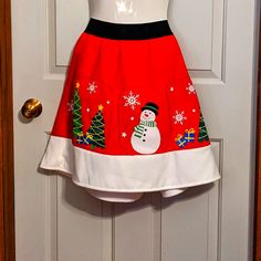 a red and white dress with a snowman on the front is hanging from a door