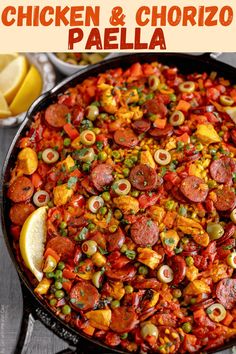 a pan filled with chicken and chorizo paella next to lemon wedges