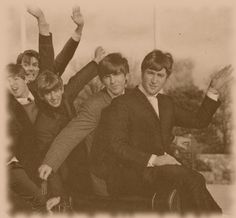 a group of young men sitting next to each other in front of a building with their hands up