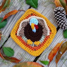 a crocheted turkey sitting on top of a wooden table next to some leaves