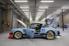 an old race car is parked in a garage with its door open and the hood up