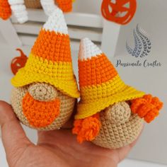 a hand holding two crocheted pumpkins with orange and white hats on them