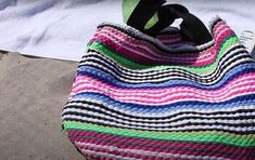 a multicolored crocheted bag sitting on the ground next to a towel