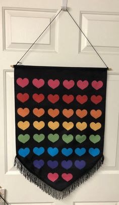 a black wall hanging with colorful hearts and fringes on the front door, next to a white door