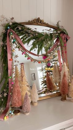 a decorated mantle with christmas trees and garland on it, in front of a mirror