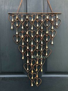 a heart shaped wall hanging with bells attached to the side of a door, on a chain