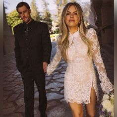 the bride and groom are holding hands as they walk down the street in their wedding attire