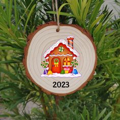 a wooden ornament with a house on it hanging from a christmas tree branch