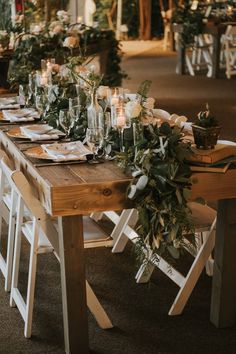 a long wooden table with candles and greenery on the top is surrounded by white chairs