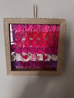 a wooden frame with pink and red flowers in it hanging on a wall next to a white wall