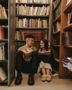 a man and woman sitting on the floor in front of a bookshelf reading