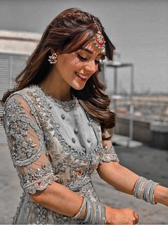 a woman in a silver dress holding something with both hands and smiling at the camera