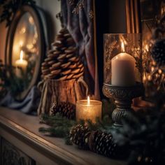 candles are lit on a mantle with pine cones