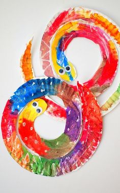 three colorful paper plates with faces and eyes in the shape of snake's tails