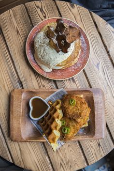 two plates with waffles and other food on them sitting on a wooden table