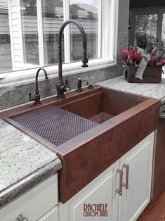 a kitchen sink sitting under a window next to a counter top with flowers on it