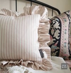 two pillows are on a bed with pink and white striped sheets, one has ruffled edges